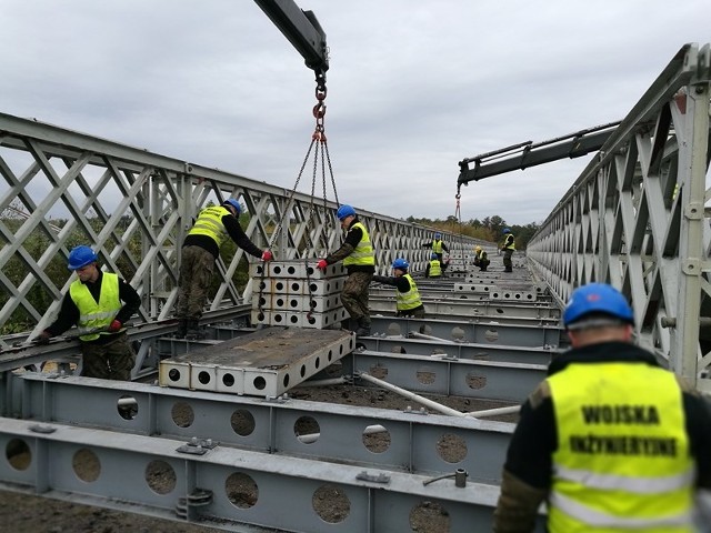 Dzięki żołnierzom z 2. Inowrocławskiego Pułku Inżynieryjnego mieszkańcy Ostrołęki i okolic mogą bez większych problemów pokonywać rzekę Narew. 3 października br. saperzy ze zgrupowania zadaniowego sformowanego na bazie 2. IPInż przystąpili do budowy dwóch mostów z konstrukcji DMS-65 o łącznej długości 240 metrów. - Zadanie w ramach szkolenia specjalistycznego wykonywały trzy grupy - montażowa, budowy podpór oraz grupa transportowa - relacjonuje dowódca kpt. Łukasz Kowalik. Na postawienie obu konstrukcji żołnierze z Inowrocławia mieli czas do końca października br. Z pracami uwinęli się kilka dni przed terminem. Montaż drugiego, ostatniego z mostów zakończył się bowiem 25 października. - Prace szły sprawnie ze względu na dobre wyszkolenie żołnierzy - podkreśla st. sierż. Dariusz Sopoliński, dowódca grupy montażowej. Budowa obu przepraw trwała 17 dni roboczych. Każdego z nich specjaliści w mundurach pracowali po 10 godzin. Utrudnieniem w budowie podpór był wysoki stan Narwi. - Żołnierze musieli przykręcać śruby w wodzie - dodaje st. chor. sztab. Dariusz Nowak, dowódca grupy budowy podpór. Zgodnie z umową wojsko musiało zamontować sześć podpór. Operacja prowadzona była w większości z promu zbudowanego z bloków parku pontonowego. - Transport elementów odbywał się zgodnie z harmonogramem dostaw. Ewentualne zmiany korygowaliśmy na bieżąco - zauważa kpr. Bartosz Budny, dowódca grupy transportowej. Do montażu użyto dziesięć tysięcy elementów o łącznej masie pięciuset ton. Żołnierze nie kryją, że budowa dwóch mostów była dużym wyzwaniem, które pozwoliło na zdobycie nowych doświadczeń z zakresu współpracy z organami administracji samorządowej, jak i z firmami budowlanymi, które muszą obecnie "podciągnąć" do obu przepraw drogi dojazdowe. Łącznie w zgrupowaniu "Ostrołęka" uczestniczyło 34 żołnierzy wraz z odpowiednim sprzętem technicznym. Jak wspomnieliśmy, budowa obu mostów została zakończona przed terminem. Dzięki wysokim kwalifikacjom i profesjonalizmowi żołnierzy 2. IPInż utrzymane zostało sprawne funkcjonowanie Ostrołęki. (FI)