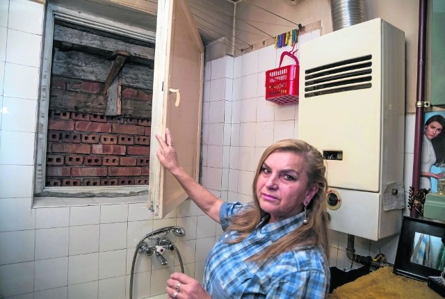Joanna Kamińska pokazuje okno w łazience i ścianę garażu, który jest źródłem  problemów w jej mieszkaniu