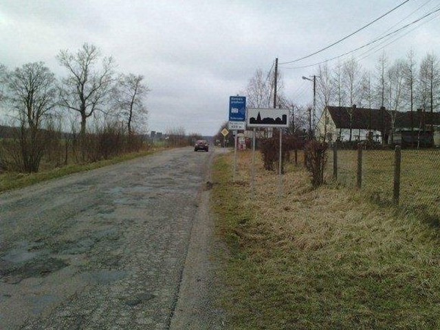 Na pierwszym planie dziurawa droga Kluki &#8211; Słupsk koło Gąbina, w tle znak "obszar zabudowany&#8221; i nowy znak zapowiadający, że będą się tutaj odbywać kontrole prędkości. 