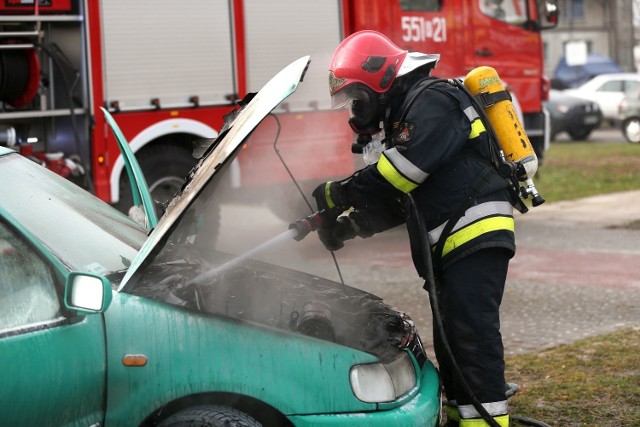 Gaszenie pożaru pod maską samochodu wodą z węża.