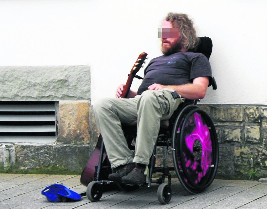 Mężczyzna grając na gitarze i siedząc na inwalidzkim wózku...