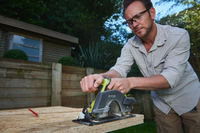 Mężczyzna przed domem używa narzędzia akumulatorowego RYOBI do cięcia drewna