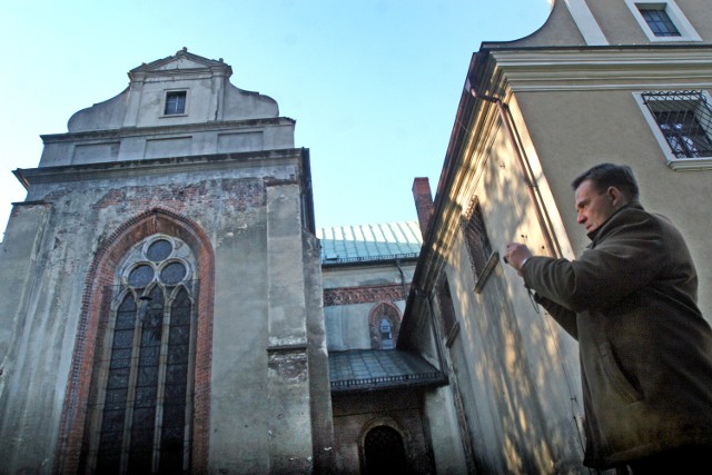 Ksiądz Rafał Wyleżoł fotografuje sypiącą się ścianę bazyliki w Rudach. Tynk spada na ziemię. Ściana nie była remontowana od II wojny światowej. Ten fragment kościoła ukryty jest w parku