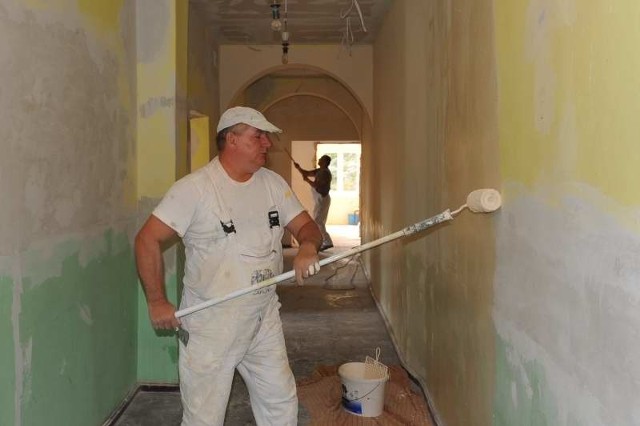Zdzisław Michalski maluje ściany w korytarzu na piętrze budynku podkładem w beżowym kolorze. Właściwa barwa ścian będzie waniliowa.