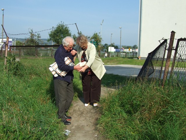 Krok po kroku Jan Olszyński wyprowadza swoją żonę przez dziurę w ogrodzeniu ścieżką wydeptaną przez ludzi, którzy w podobny jak oni sposób chcieli uniknąć 3 zł opłaty za samochód