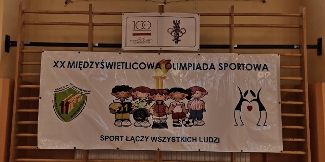 Plakat XXMiędzyświetlicowej Olimpiady Sportowej na drabinkach w hali sportowej.