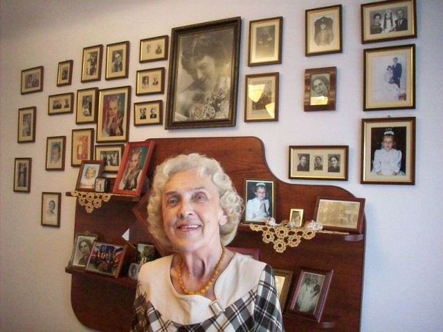 Krystyna Łukasik na tle ściany pamięci, zdjęć swojej rodziny.                      