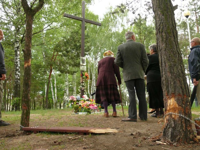 Systematycznie przy krzyżu grupa osób spotyka się na modlitwie. Z przodu zniszczona ławka.