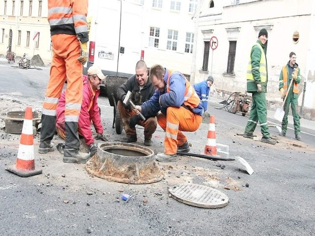 Pracownicy firmy "Spec-dróg" poziomują studzienki do wysokości asfaltu