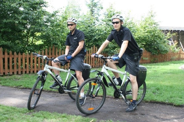 Rowerzysci ubrani są w czarne lub białe koszulki z napisem "policja", krótkie spodenki i białe kaski
