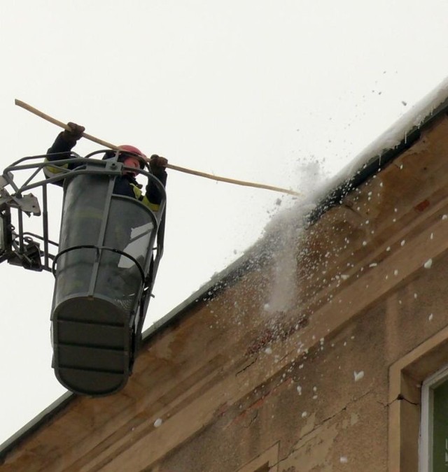 Strażak w akcji strącania śniegu z dachu.