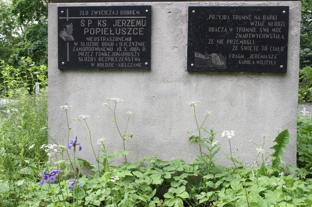 Wokół tablicy poświęconej pamięci księdza Jerzego Popiełuszki na cmentarzu starym w Kielcach, rosną pokaźne chwasty.