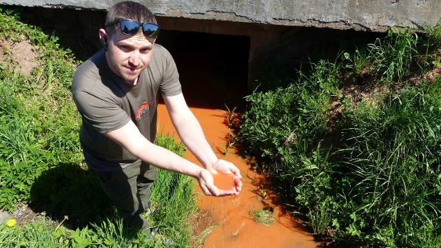 Z kopalni Baranów w Suchedniowie do rzeki Kamionki strumieniem leje się woda z dużą ilością gliny. Na zdjęciu Krzysztof Rózga pokazuje, jaki kolor ma woda ze zrzutu.