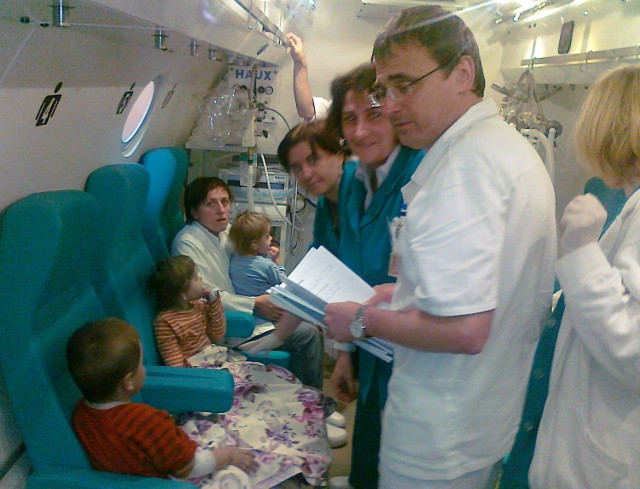 Dzieci z matką i personelem medycznym w komorze hiperbarycznej.