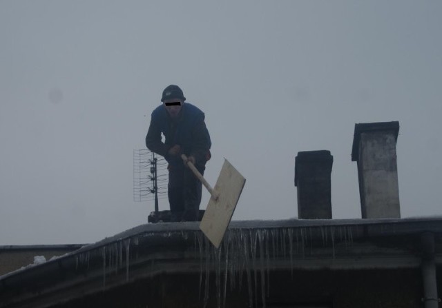 Pracownik odśnieża dach bez żadnego zabezpieczenia.