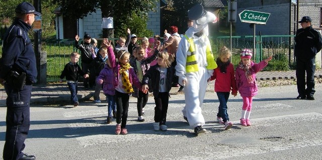 Koziołek Spoko przeprowadza dzieci przez jezdnię w Krasocinie w asyście miejscowych dzielnicowych.