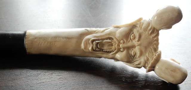 Laska z polakierowanego na czarno drewna z uchwytem kościanym w postaci dwustronnej maski zwieńczonej miniaturową głową i miniaturową czaszką
