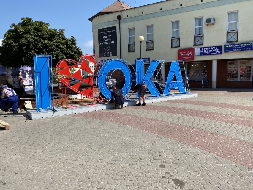 Ostrołęka. I love OKA - montaż napisu świetlnego przy scenie pomiędzy domami handlowymi, 16.08.2021