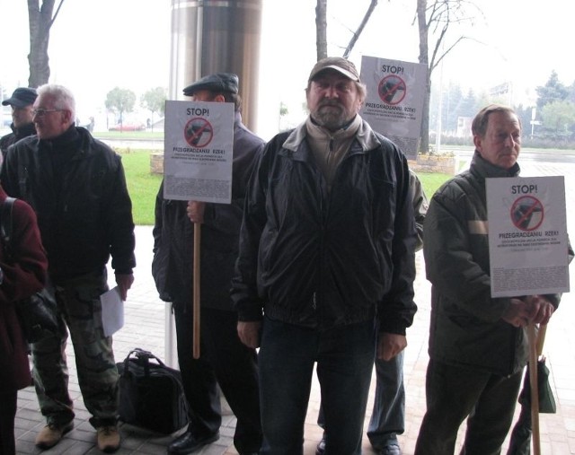 Pikietujący przed Urzędem Marszałkowskim w Rzeszowie przynieśli plakaty z napisem "Stop przegradzaniu rzek&#8221;.