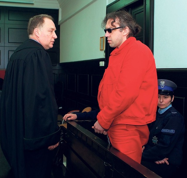Oskarżony - w czerwonym drelichu dla szczególnie niebezpiecznych przestępców - w czasie rozprawy rozmawia ze swoim obrońcą.
