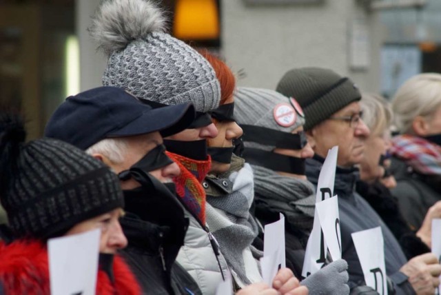 Uczestnicy z oczami i ustami zakrytymi czarnymi przepaskami ustawili się w rzędzie, trzymając napis "Skradziona sprawiedliwość Poznań".