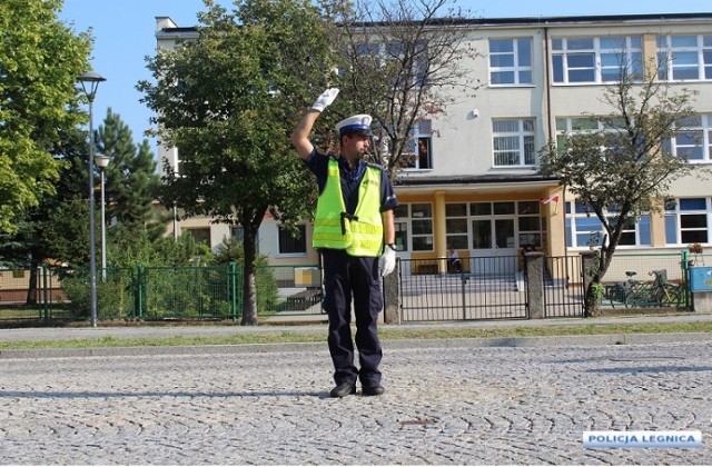 Na zdjęciu policjant ma uniesioną rękę do góry i sygnalizuje tym gestem zakaz wjazdu i wejścia na skrzyżowanie. Nawet, gdy na sygnalizacji świetlnej jest zielone światło to zabroniony jest wjazd i wejście na skrzyżowanie. Pamiętaj, że gesty policjanta kierującego ruchem mają pierwszeństwo przed sygnalizacją.