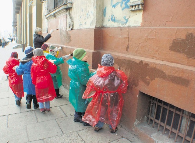 Dzieci ubrane w kolorowe foliowe płaszcze i w rękawiczkach z zapałem zamalowywały napisy i rysunki szpecące gmach ich przedszkola przy al. Kościuszki.