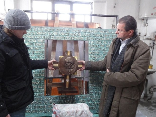 Piotr Prus z dyrektorem Pawłem Pieniężnym przymierzają relikwiarz do tablicy na której znajdują się fragmenty testamentu Jana Pawła II