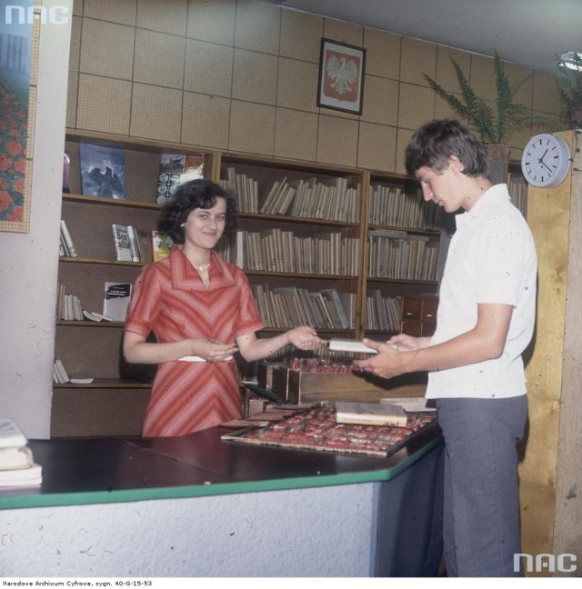 Bibliotekarka i czytelnik w bibliotece. W tle widoczne godło państwowe - 1979-06-22
