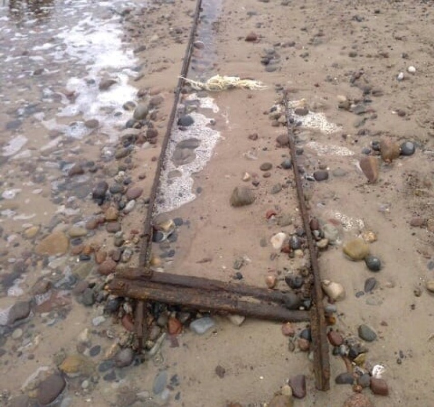 Fragment dawnego toru wyłania się z piasku na plaży między...