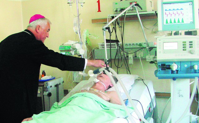 Biskup Jan Szkodoń błogosławi znakiem krzyża pacjenta oddziału intensywnej opieki medycznej