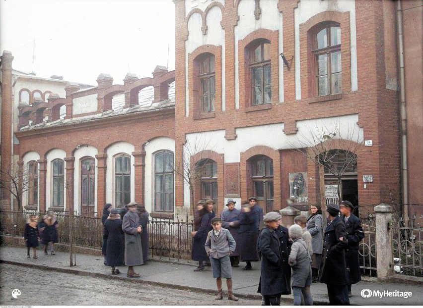 Fragment ulicy. Widoczni przechodnie, na budynkach szyldy...