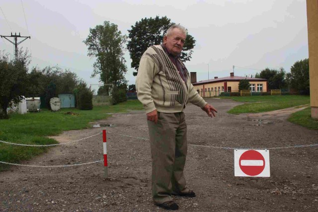 Stanisław Antończak pokazuje znak zakazu wjazdu. W  tle widać przedszkole