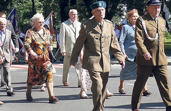 Poczty sztandarowe, kombatanci i młodzież maszerują na cmentarz wojskowy w Rawie