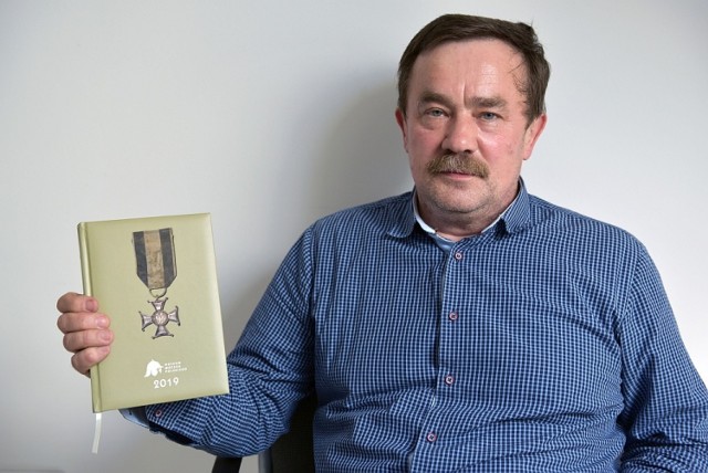 Jan Ruchała prezentuje okolicznościowy kalendarz z Krzyżem Virtuti Militari Józefa Kustronia z zakrwawioną wstążką