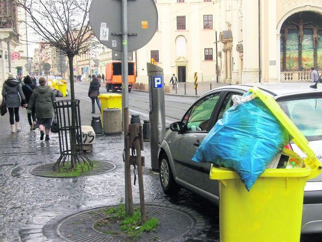 System dalej szwankuje. Grudzień, godz. 11, ul. Karmelicka. Kubły wypchane odpadami ciągle stoją. Mijają je tłumy przechodniów i turystów. Samochód firmy wywozowej (w tle) dopiero jedzie po śmieci.