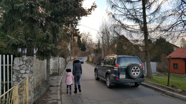 Ulica Jodłowa. Piesi nie mają chodnika, a auta jadące z naprzeciwka ledwo mieszczą się koło siebie