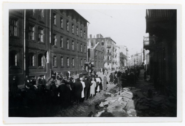 Warszawa. Ul. Srebrna. Zakłady „Bormann, Szwede i spółka, skrzyżowanie z ul. Wronią, w oddali kamienice przy ul. Twardej. Na ulicy tłum ludzi, stojący w kolejce (być może w związku ze zwężeniem ulicy barykadą nieopodal ul. Miedzianej.