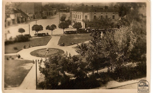 Fotografia wykonana w okresie powojennym ukazuje skwer na placu Strażackim z ukrytym wśród drzew Pomnikiem Wdzięczności oraz fragment placu Kilińskiego przed przebudową.