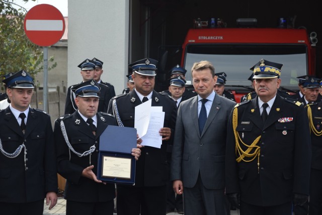 Minister Błaszczak w towarzystwie kobylińskich strażaków, którzy trzymają w rękach dokument promesy o wartości 595 tys. zł na zakup nowego średniego wozu bojowego. 20.09.2017 r.