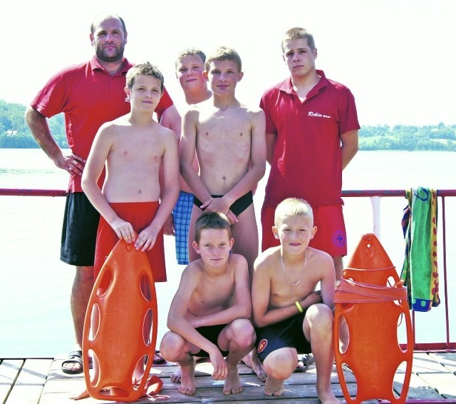 Na zdjęciu z ratownikami grupa dzieci, która bierze udział w codziennych kursach pływania.