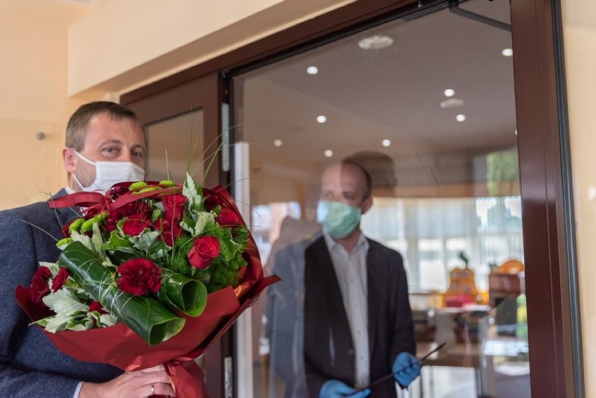 Zastępca burmistrza w maseczce i rękawiczkach z kwiatami w bibliotece