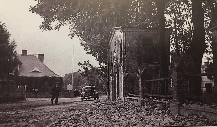Lata 1920-1940, Brama do kościoła parafialnego wraz z dzwonnicą, zniszczona przez Niemców na początku II WŚ.W tle budynek, obecnie Gminny Ośrodek Kultury, przebudowany w latach 80 XX w.