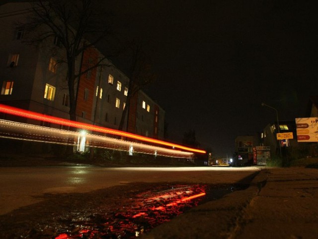 Nocą kielecką ulicę Okrzei oświetlają jedynie światła przejeżdżających samochodów.