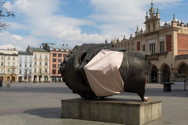 Najważniejsze symbole roku pandemii w Polsce - pusty Rynek Główny w Krakowie oraz maseczka. Tu na rzeźbie Igora Mioraja