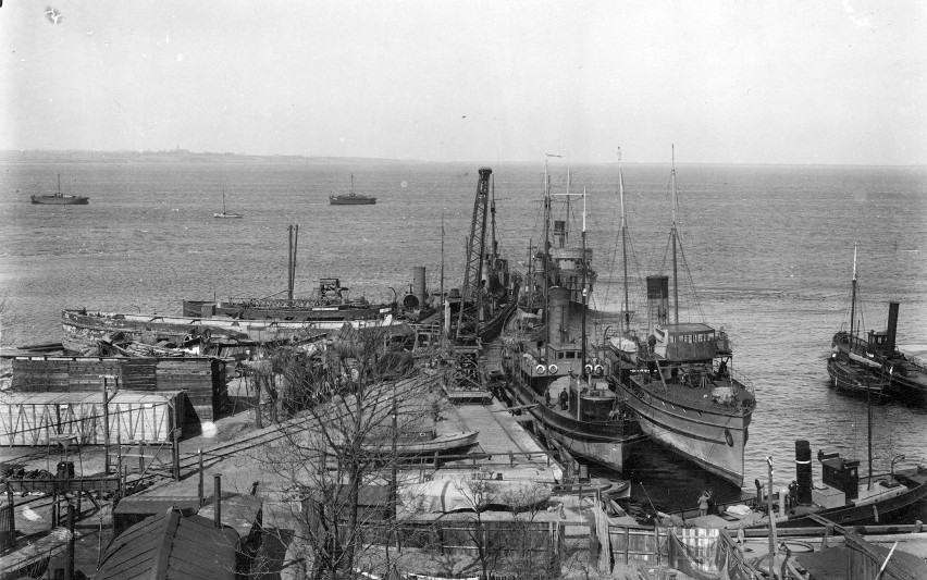 Kutry rybackie i okręty wojenne stojące w porcie w Pucku - widok z góry. Pośrodku, zacumowany przy nabrzeżu, stoi okręt hydrograficzny ORP „Pomorzanin”, obok niego z prawej kanonierka ORP „Generał Haller”. W tle ORP „Komendant Piłsudski” (fot. i opis NAC)