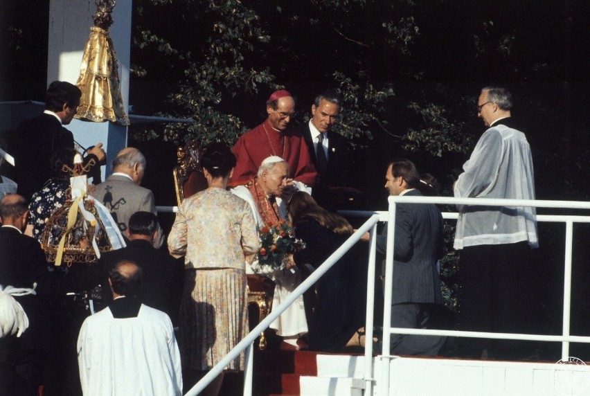 Jan Paweł II przyjmuje dary od wiernych siedząc na tronie...