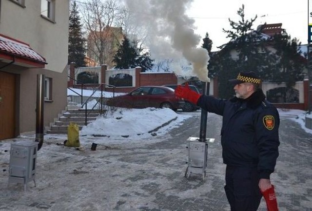 Bogusław Kmieć z ekopatrolu Straży Miejskiej pokazuje jak rozpalić ogień w piecu. Na zdjęciu z lewej strony - koza prawidłowo rozpalona daje niewielką ilość dymu. Po prawej stronie z urządzenia wydobywa się duża ilość gryzącego dymu ponieważ rozpalono je niewłaściwie.