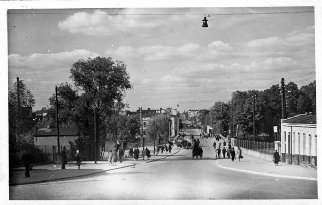 Centrum Tomaszowa, 1943 r.  Niby nic złego się nie dzieje, ludzie spacerują jak dawnej... ale obok jest głód, choroby, łapanki, wywózki do Oświęcimia, na roboty przymusowe, uliczne egzekucje...