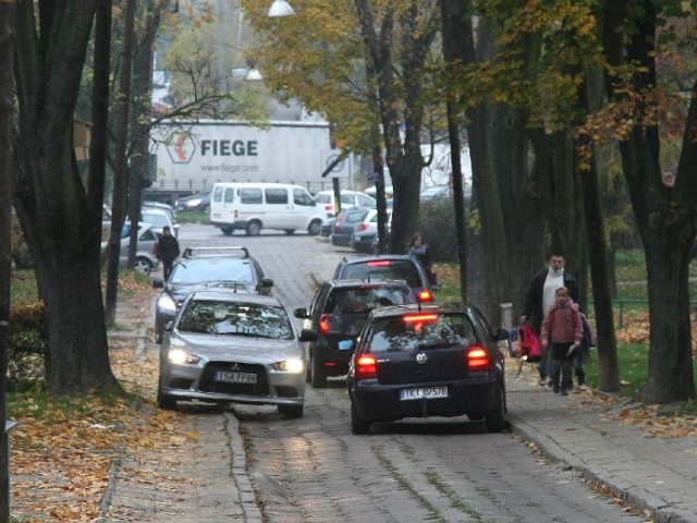 Chodnikiem, na który wjeżdżają samochody, aby się minąć chodzą dzieci do szkoły.